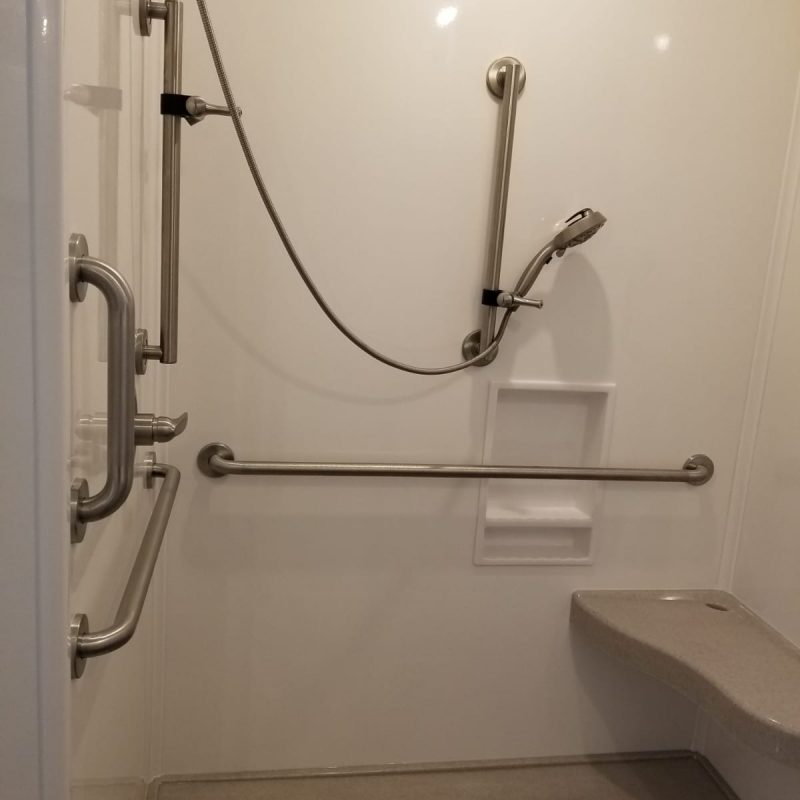 Shower interior with various grab bars, built-in shower seat, and recessed soap caddy.